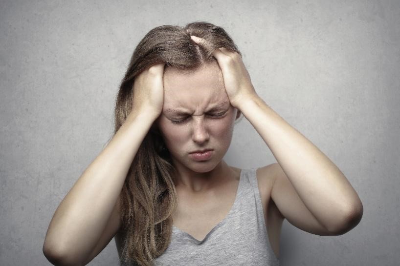 A person in a grey tank top holding their head in stress.