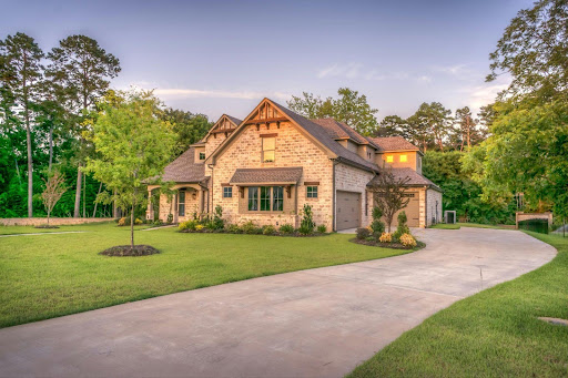 A beautiful modern brick home with a curved interlock driveway surrounded by lush green landscaping and tall trees in the background, displaying one of the many interlock designs available.